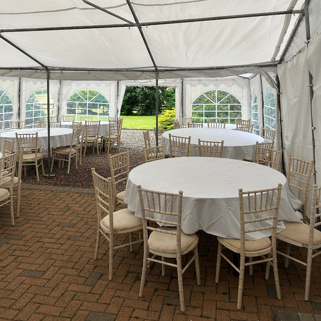 Outdoor setting with white tents, round tables, and wooden chairs on a brick patio.