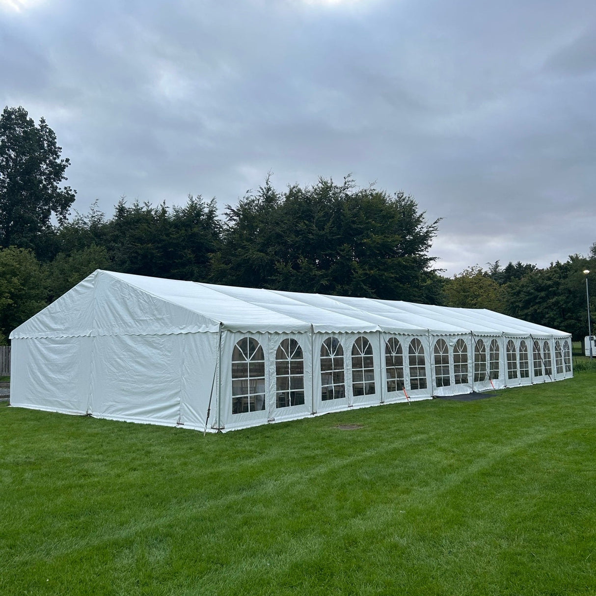 Long white tent on a grassy field with trees in the background