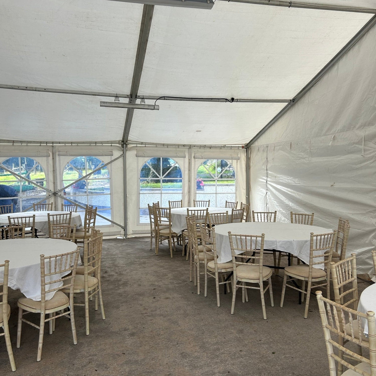 White chairs and tables set up under a large white tent on a concrete surface.