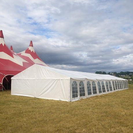 Large 9x36 meter white marquee tent on grass with red and white striped tent in the background