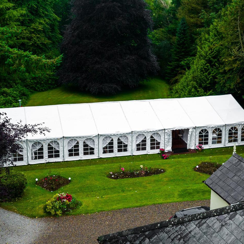 Large white tent on a grassy area surrounded by trees