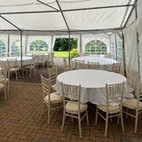 Outdoor setting with white tents, round tables, and wooden chairs on a brick patio.