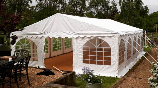 White party tent set up outdoors with tables and chairs around it.
