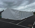 Long 9x21 meter white tent structure on a dark asphalt surface with a cloudy sky.
