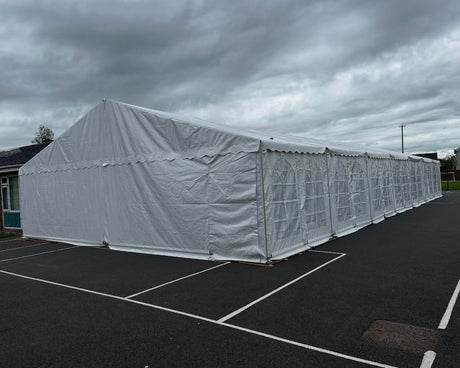 Long 9x21 meter white tent structure on a dark asphalt surface with a cloudy sky.