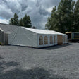 White tent with arched windows on a gravel surface under a cloudy sky.