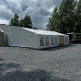 White tent with arched windows on a gravel surface under a cloudy sky.