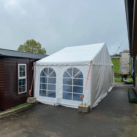White 9x3 meter marquee tent with arched windows next to a brown building on a cloudy day.