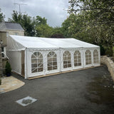 White marquee tent set up outdoors on a driveway with trees and a house in the background.