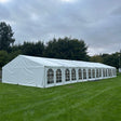 Long white tent on a grassy field with trees in the background