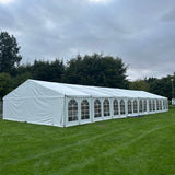 Long white tent on a grassy field with trees in the background