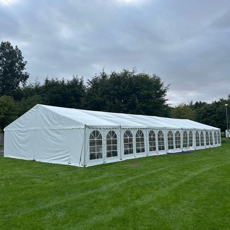 Long white tent on a grassy field with trees in the background