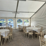 White chairs and tables set up under a large white tent on a concrete surface.