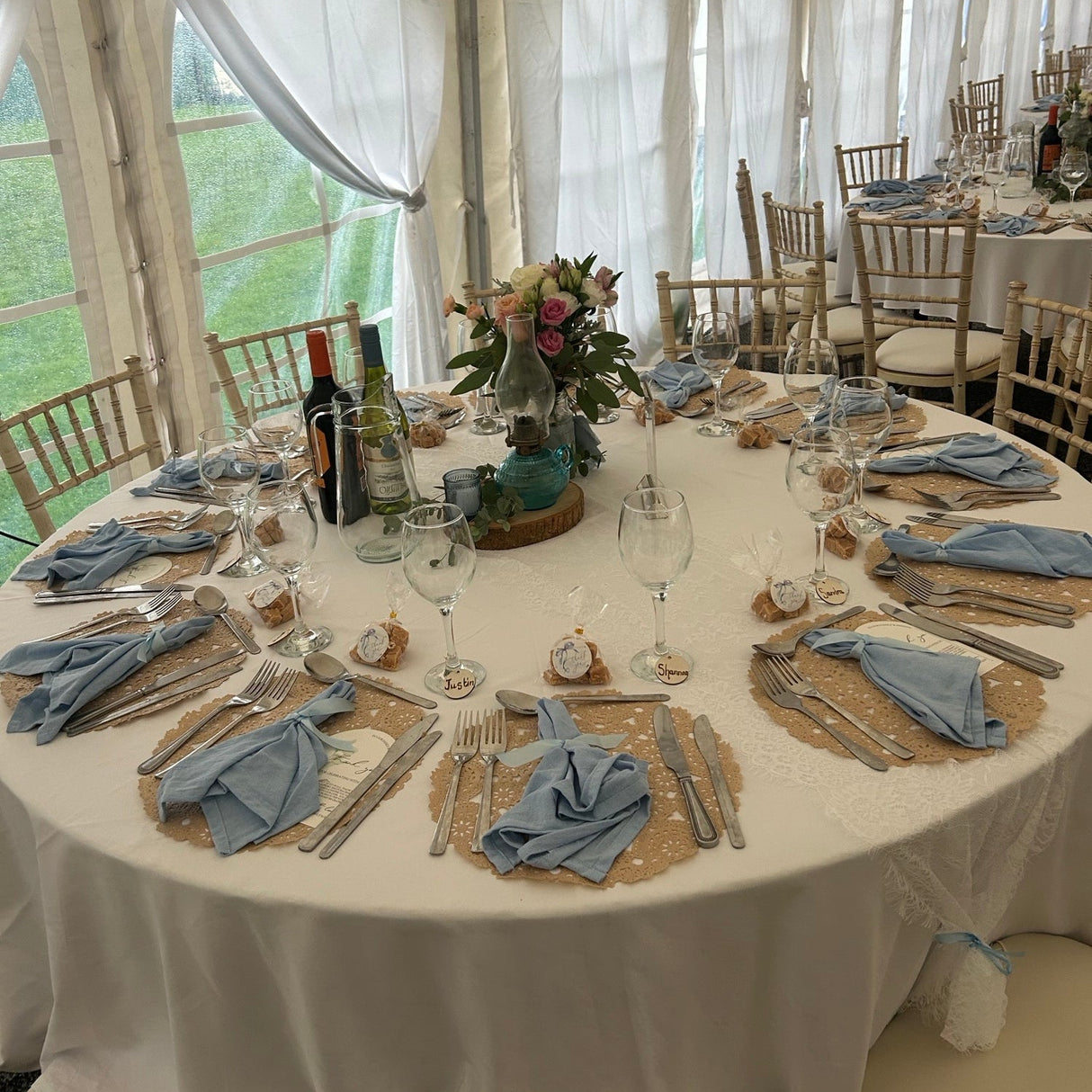 Round table set for a formal event with white tablecloth, blue napkins, and floral centerpieces.