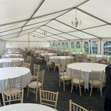 Large indoor event space with white tables and chairs under a white tent.