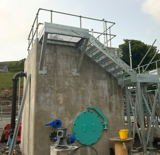 Industrial setup with concrete structure, metal stairs, and various equipment on a cloudy day.